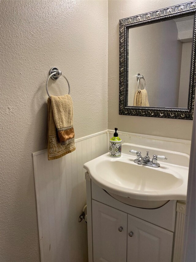 bathroom with wainscoting, vanity, and a textured wall