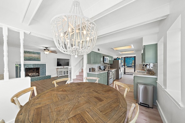 dining area with light wood finished floors, ceiling fan with notable chandelier, visible vents, and a tile fireplace