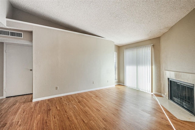 unfurnished living room with a textured ceiling, a fireplace with raised hearth, visible vents, and wood finished floors