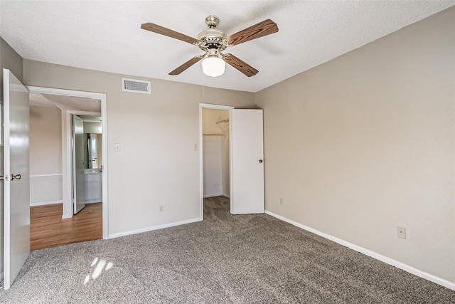 unfurnished bedroom featuring visible vents, carpet flooring, a ceiling fan, a walk in closet, and baseboards
