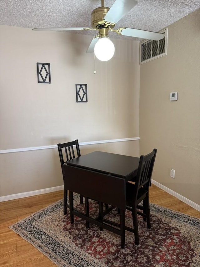 dining room featuring wood finished floors, a ceiling fan, a textured ceiling, visible vents, and baseboards