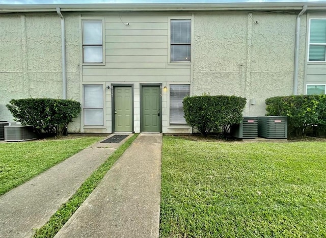 view of front of property with a front yard, cooling unit, and stucco siding