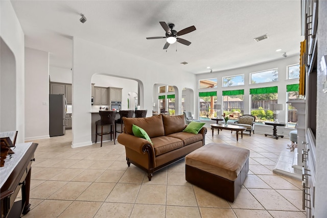 15306 Clearhaven Ct, Cypress, TX 77429 - living room featuring a fireplace, visible vents, ceiling fan, arched walkways, and light tile patterned flooring