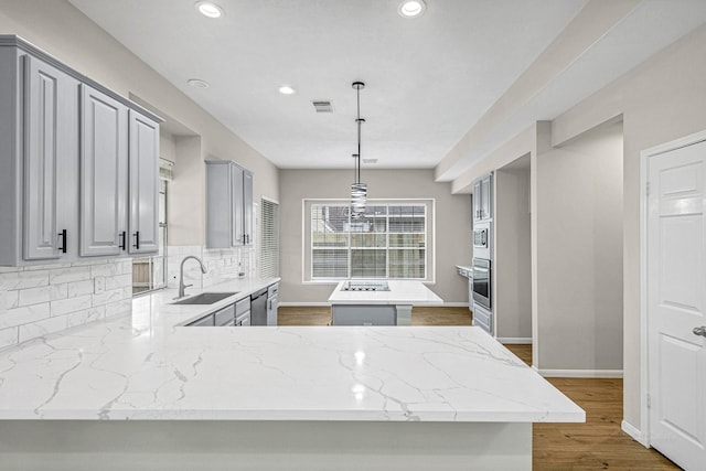 kitchen with a center island, a sink, gray cabinets, visible vents, and backsplash