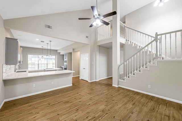 unfurnished living room featuring stairs, wood finished floors, high vaulted ceiling, visible vents, and a ceiling fan