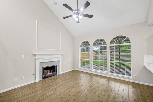 unfurnished living room featuring wood finished floors, high vaulted ceiling, a tiled fireplace, baseboards, and ceiling fan