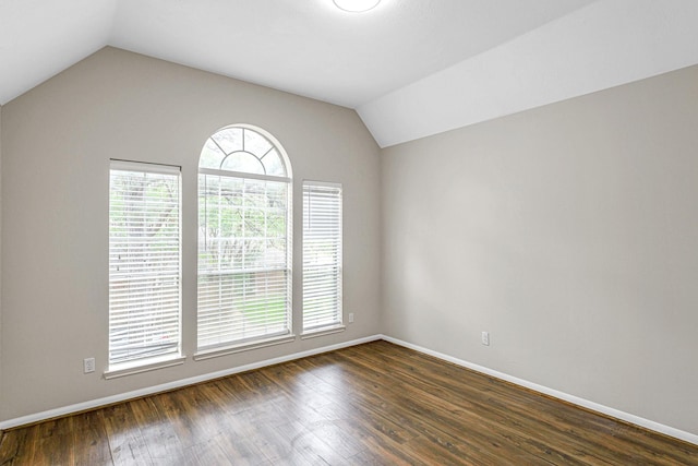 empty room with vaulted ceiling, dark wood-style flooring, and baseboards