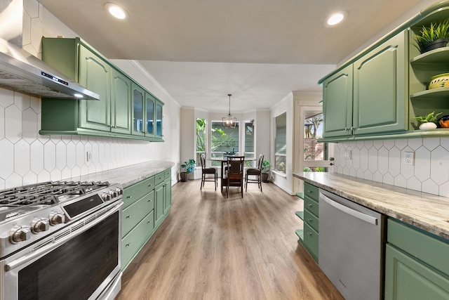 kitchen with appliances with stainless steel finishes, wall chimney range hood, green cabinets, open shelves, and light wood-type flooring
