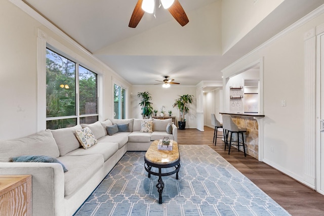 living area with ceiling fan, vaulted ceiling, wood finished floors, ornamental molding, and baseboards