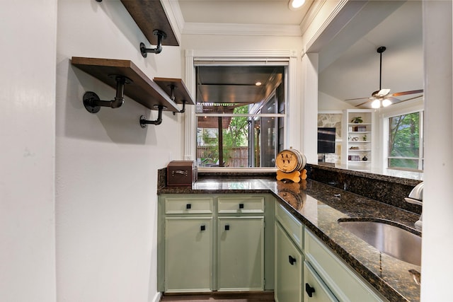 kitchen featuring green cabinetry, a sink, a ceiling fan, dark stone counters, and crown molding