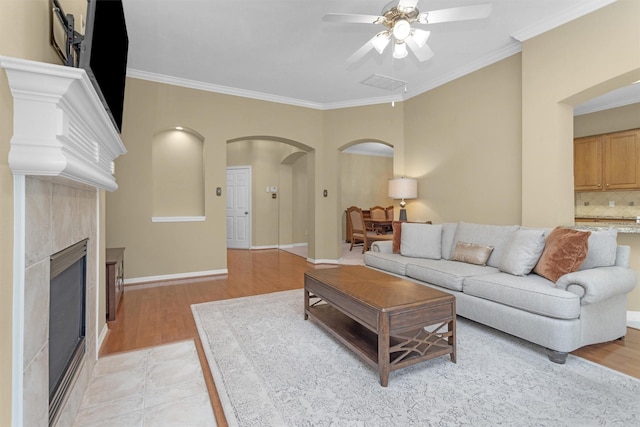 living area featuring ornamental molding, arched walkways, a ceiling fan, and light wood-style flooring