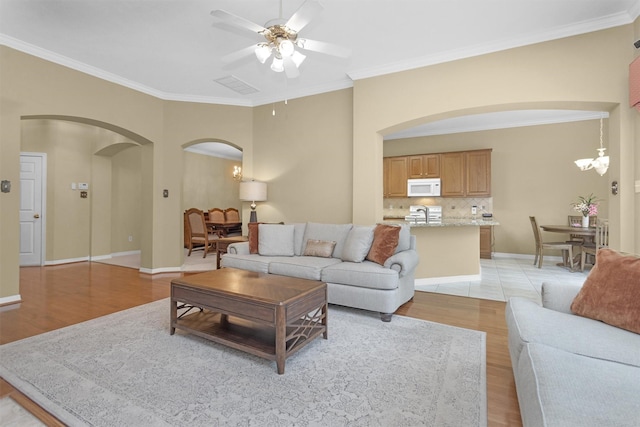 living room with ornamental molding, light wood-style floors, a ceiling fan, and arched walkways