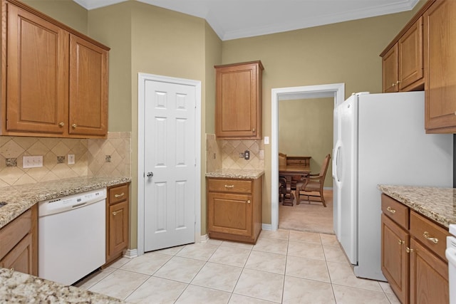 kitchen with brown cabinetry, white appliances, light stone counters, crown molding, and decorative backsplash