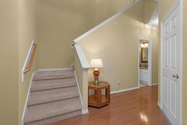 staircase featuring a high ceiling, baseboards, and wood finished floors