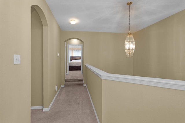 hall with light colored carpet, baseboards, and arched walkways
