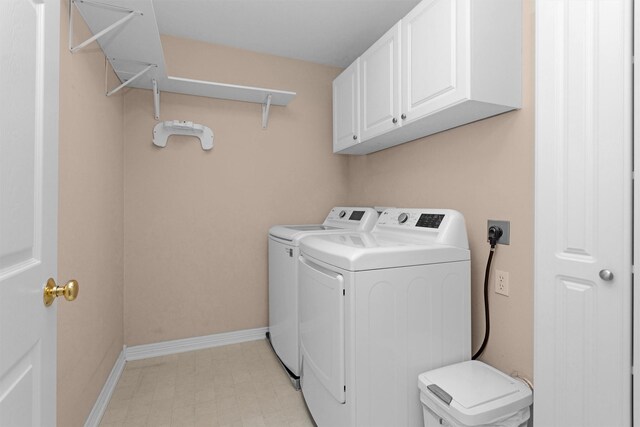 clothes washing area featuring baseboards, light floors, washing machine and dryer, and cabinet space