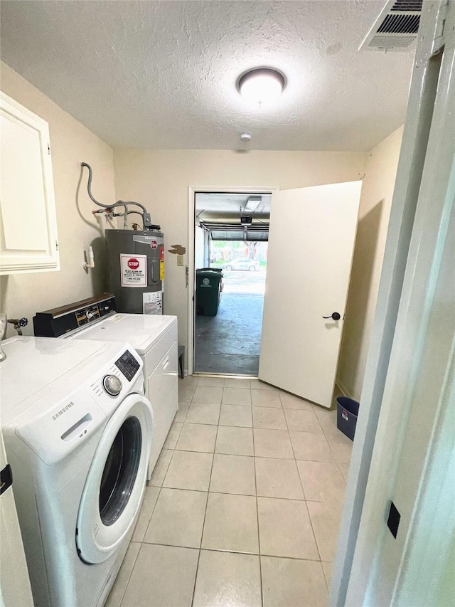 clothes washing area featuring cabinet space, water heater, a textured ceiling, washing machine and clothes dryer, and light tile patterned floors