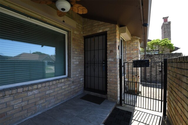 7521 Beaudelaire Cir, Galveston, TX 77551 - view of exterior entry with ceiling fan, brick siding, a gate, and fence