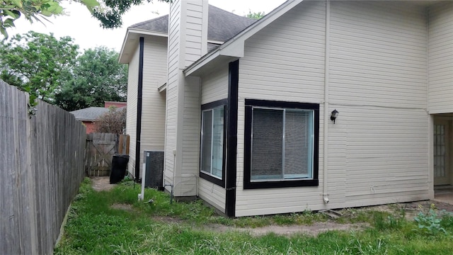 view of property exterior with a chimney, a shingled roof, and fence