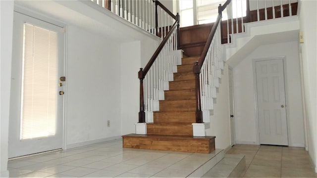 staircase with a healthy amount of sunlight, tile patterned flooring, baseboards, and a high ceiling