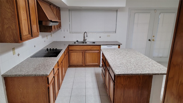 kitchen featuring brown cabinets, a sink, backsplash, premium range hood, and black electric stovetop