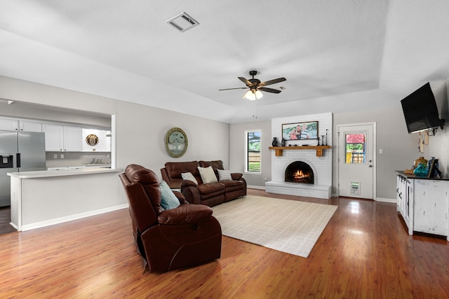 living area with baseboards, ceiling fan, visible vents, wood finished floors, and a fireplace