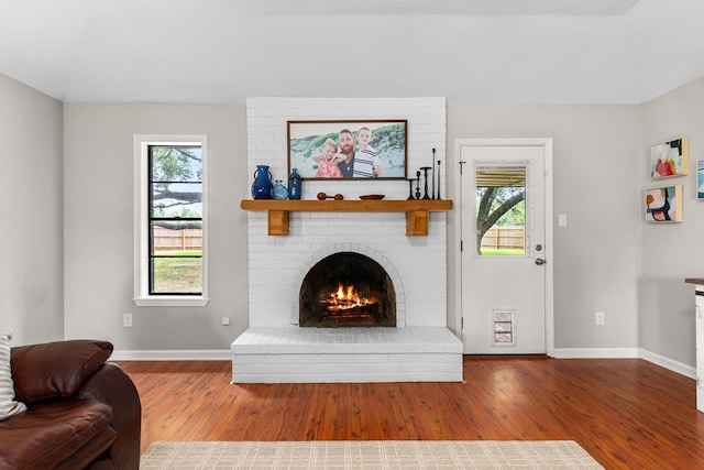 living room featuring a brick fireplace, baseboards, and wood finished floors
