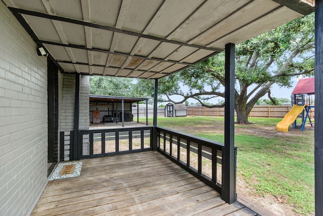 deck featuring a storage unit, an outbuilding, a fenced backyard, a lawn, and a playground