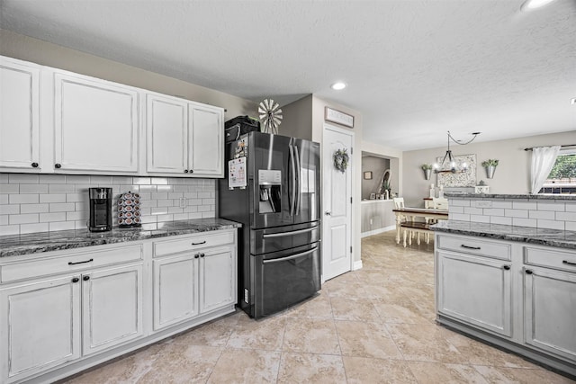 kitchen with a chandelier, decorative backsplash, fridge with ice dispenser, and dark stone counters