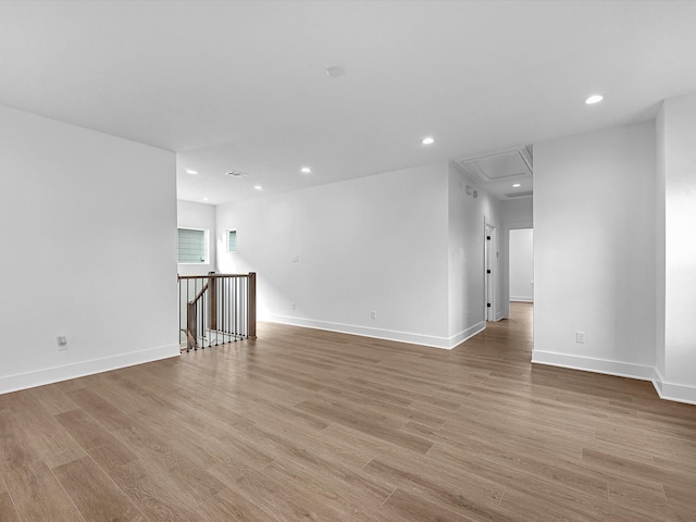 unfurnished room with recessed lighting, attic access, baseboards, and wood finished floors