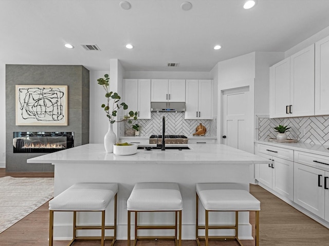 kitchen featuring under cabinet range hood, white cabinetry, a kitchen bar, and visible vents