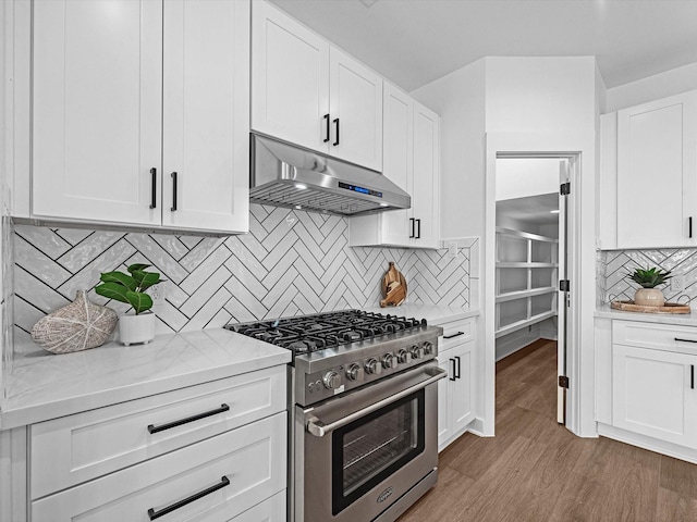kitchen featuring under cabinet range hood, high end range, white cabinetry, wood finished floors, and backsplash