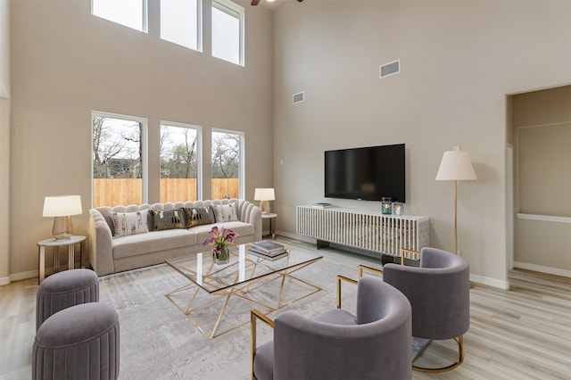 living area with a high ceiling, baseboards, visible vents, and wood finished floors