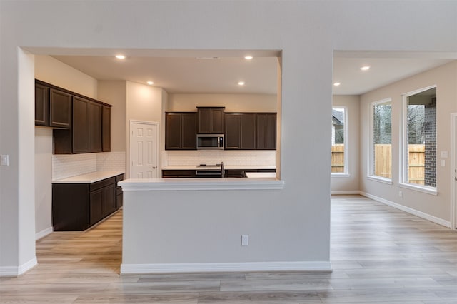 kitchen featuring tasteful backsplash, dark brown cabinets, stainless steel microwave, and light wood-style flooring