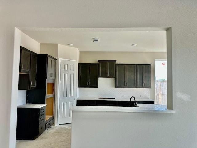 kitchen with visible vents, a sink, a peninsula, backsplash, and light countertops