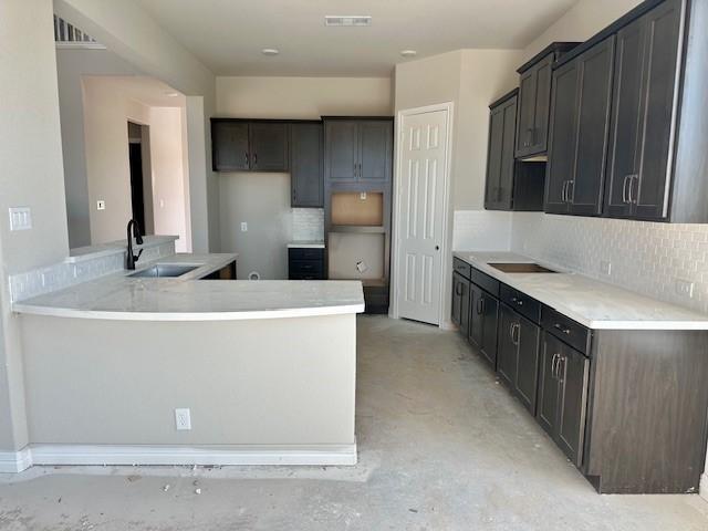 kitchen featuring a peninsula, a sink, visible vents, concrete flooring, and decorative backsplash