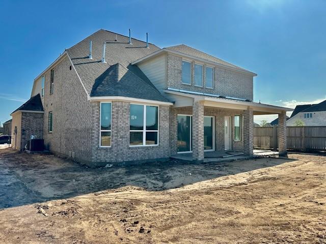 back of house with central air condition unit, roof with shingles, brick siding, and fence