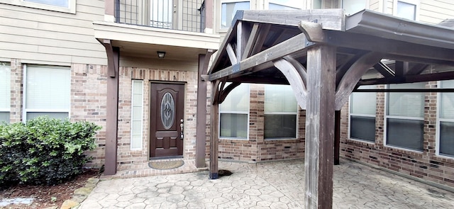 property entrance featuring a balcony, brick siding, and a patio