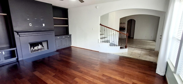 unfurnished living room with ceiling fan, wood finished floors, stairway, a fireplace, and arched walkways