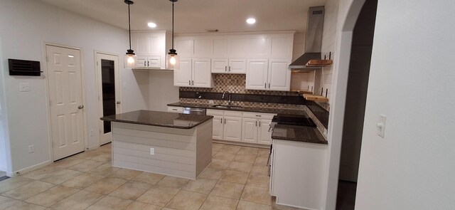 kitchen featuring wall chimney exhaust hood, tasteful backsplash, white cabinetry, arched walkways, and a center island