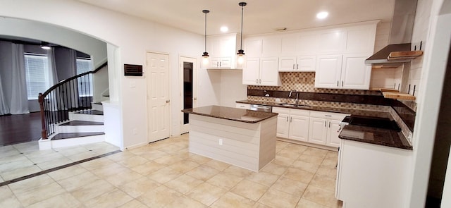 kitchen with wall chimney range hood, backsplash, a sink, a center island, and white cabinetry