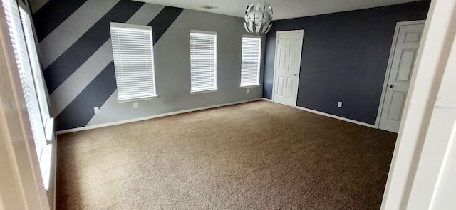 carpeted spare room featuring a chandelier and baseboards