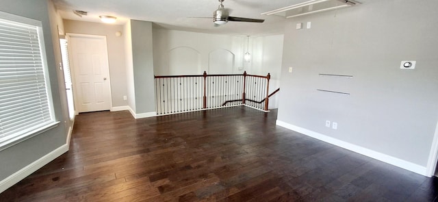 unfurnished room featuring attic access, dark wood-type flooring, ceiling fan, and baseboards