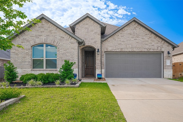 french provincial home with stone siding, a garage, a front yard, brick siding, and driveway