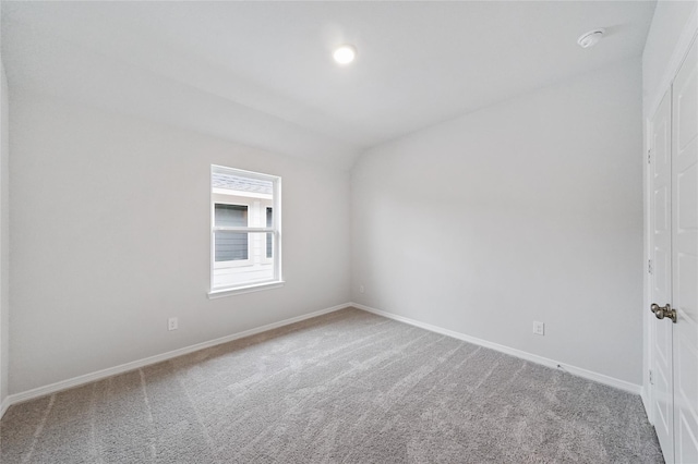 carpeted empty room with baseboards, vaulted ceiling, and a smoke detector