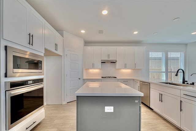 kitchen featuring appliances with stainless steel finishes, a sink, under cabinet range hood, backsplash, and light countertops
