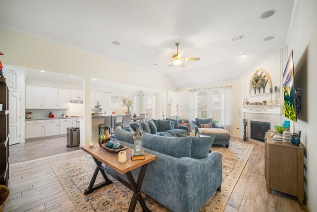 living area with crown molding, ceiling fan, a tile fireplace, light wood-style floors, and vaulted ceiling