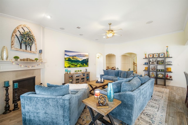 living area with ornamental molding, arched walkways, ceiling fan, wood finished floors, and a fireplace