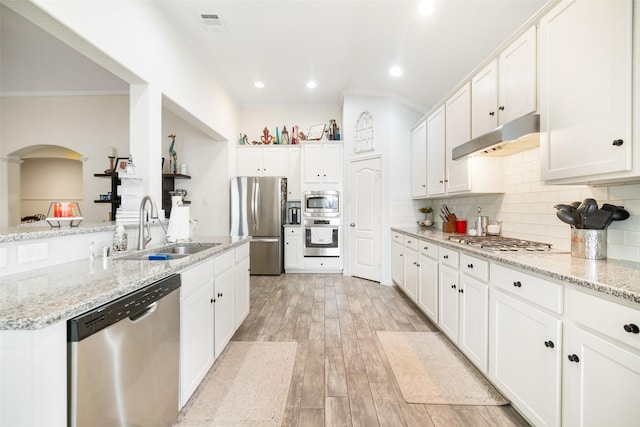 kitchen with stainless steel appliances, a sink, under cabinet range hood, crown molding, and decorative backsplash