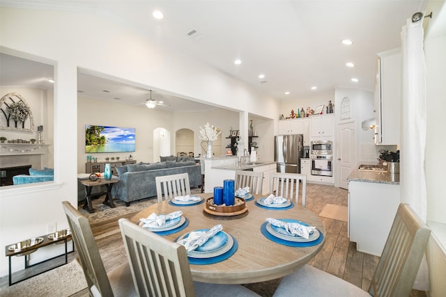 dining room with light wood-type flooring, recessed lighting, arched walkways, ceiling fan, and crown molding